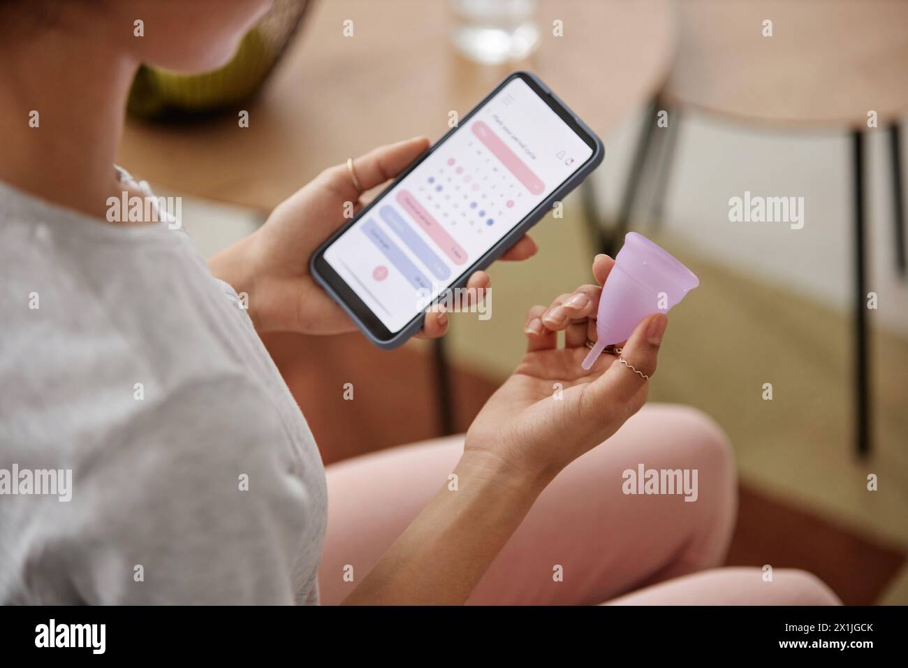 Closeup of unrecognizable girl holding menstrual cup and smartphone with period tracker app on screen copy space Stock Photo