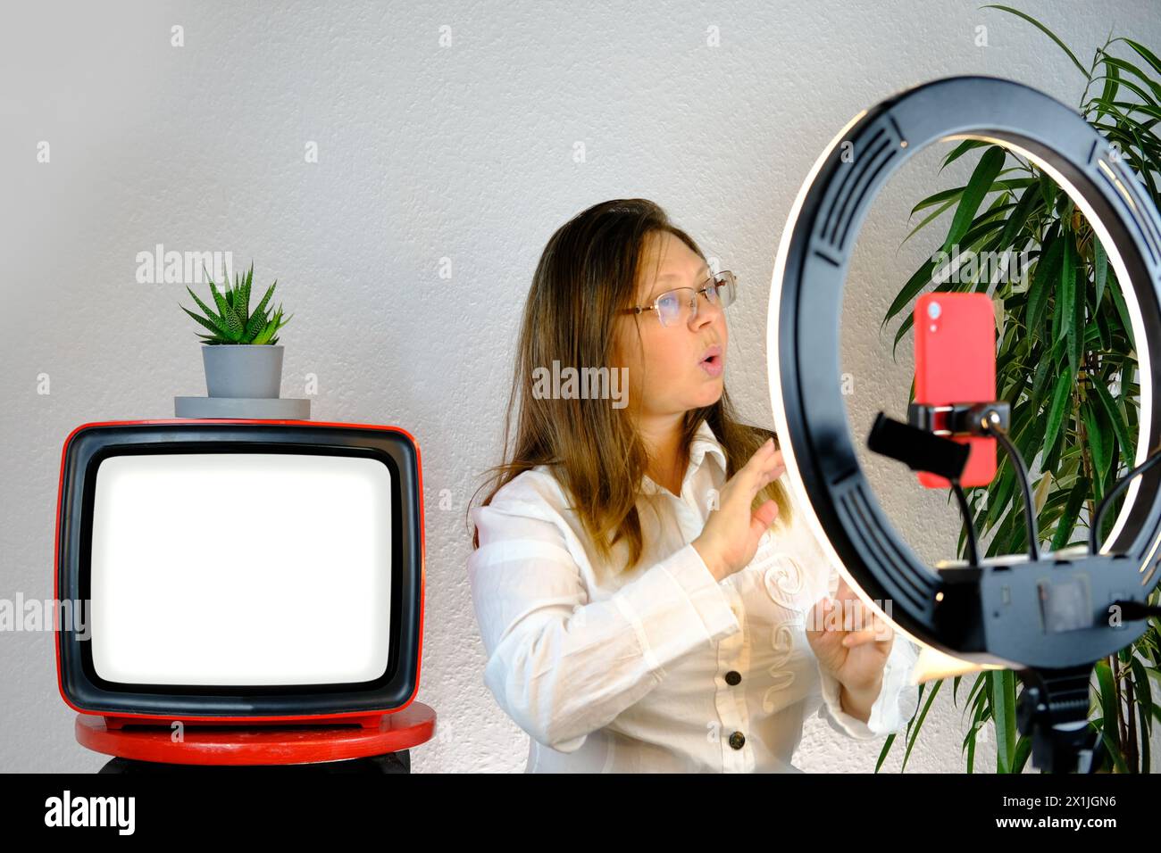 white screen, old retro analog TV, woman 45 years old, female blogger sits in front ring light and red smartphone, emotionally talks on topic of busin Stock Photo