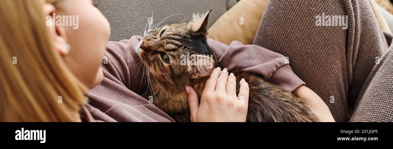 A woman with short hair sits on a sofa, gently petting a contented cat in a cozy domestic setting. Stock Photo