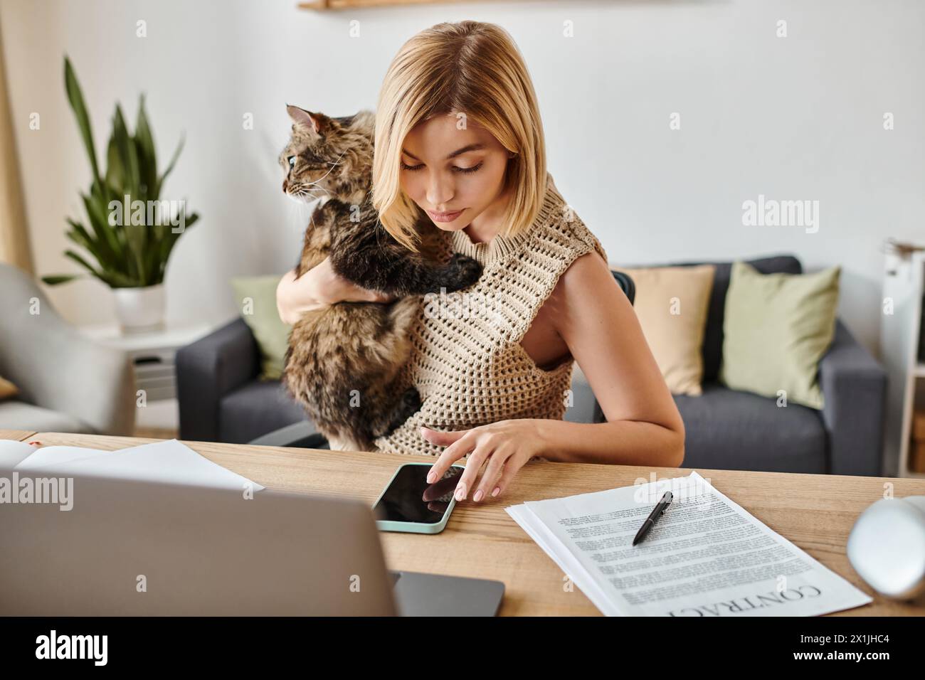 A woman with short hair sits at a table, contently petting her cat perched on her lap, creating a serene atmosphere. Stock Photo