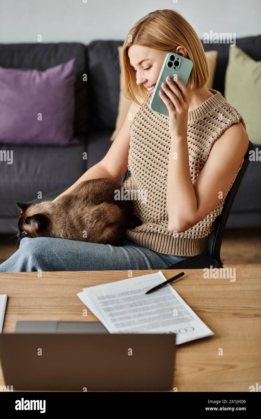 A stylish woman with short hair relaxes on a couch, focused on her cell phone while her contented cat rests on her lap. Stock Photo