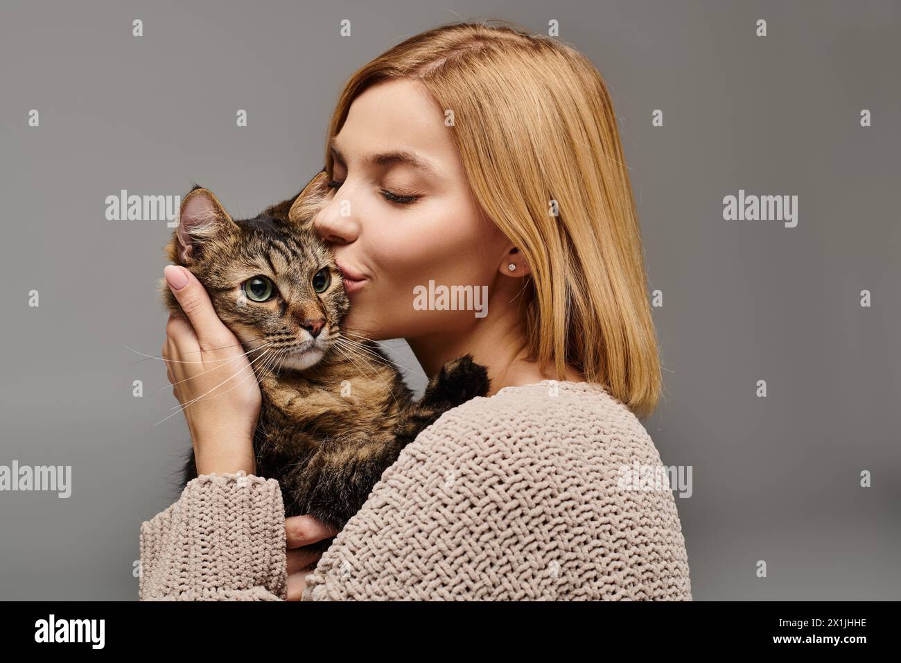 A short-haired woman tenderly cradling a cat in her hands, forming a loving bond between them at home. Stock Photo
