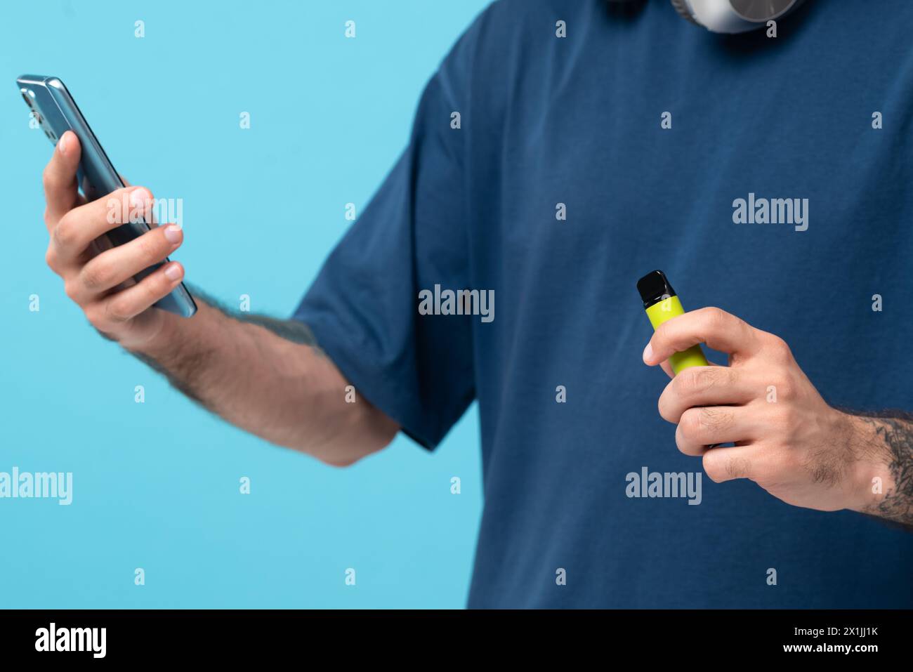 Green disposable electronic cigarette and phone in a man's hand. Modern online communication. on blue background. Stock Photo