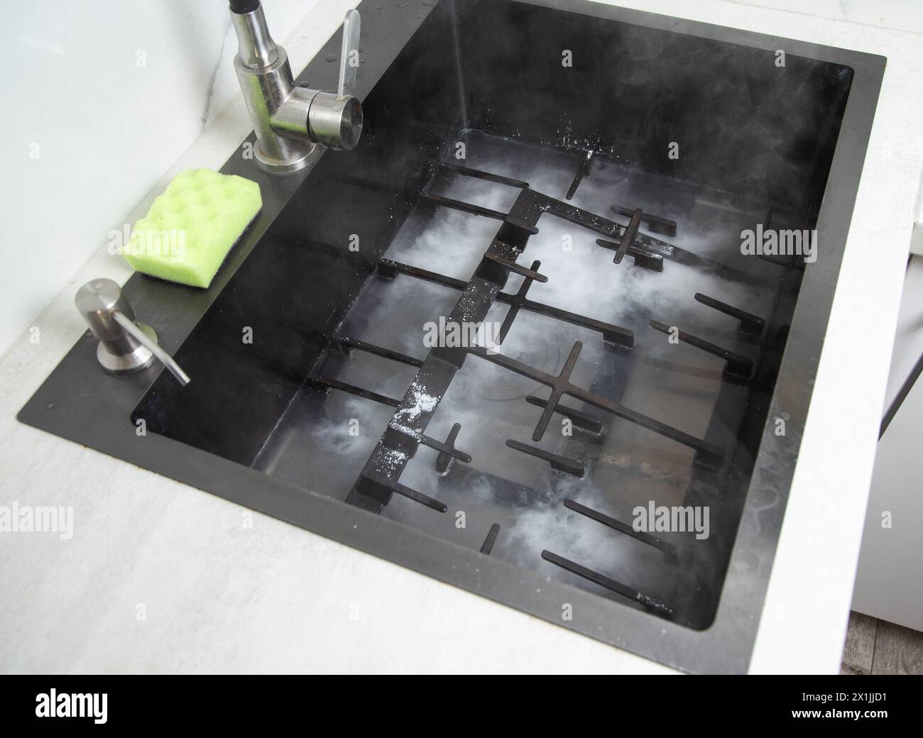 Dirty gas stove grates in the sink with a modern oxygen cleaner for
