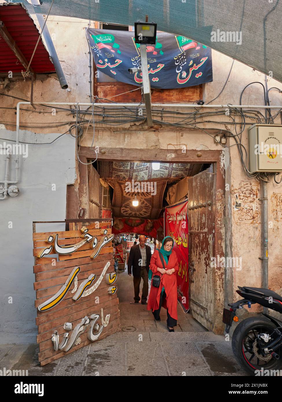 Iranian woman wearing red cloak walk in a narrow doorway in the Grand Bazaar area. Isfahan, Iran. Stock Photo