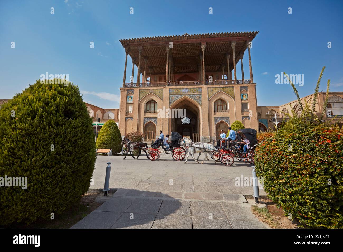 Horse drawn carriages pass by the Ali Qapu Palace in Naqsh-e Jahan Square, UNESCO World Heritage Site. Isfahan, Iran. Stock Photo