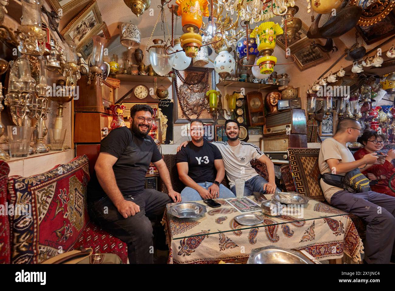 Company of young smiling Iranian men sitting together in Azadegan Cafe with its unusual interior decoration. Grand Bazaar, Isfahan, Iran. Stock Photo