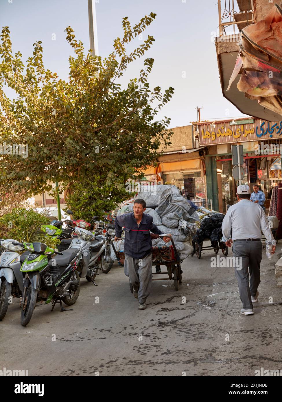 A porter pulls his heavily loaded cart in a narrow street near the Grand Bazaar of Isfahan, Iran. Stock Photo