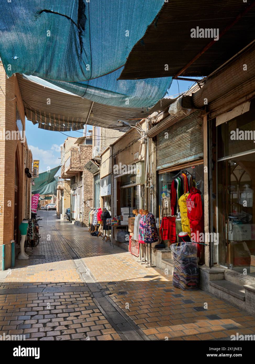 A narrow cobbled street with sun shade canopy lined with small shops in the historic center of Isfahan, Iran. Stock Photo