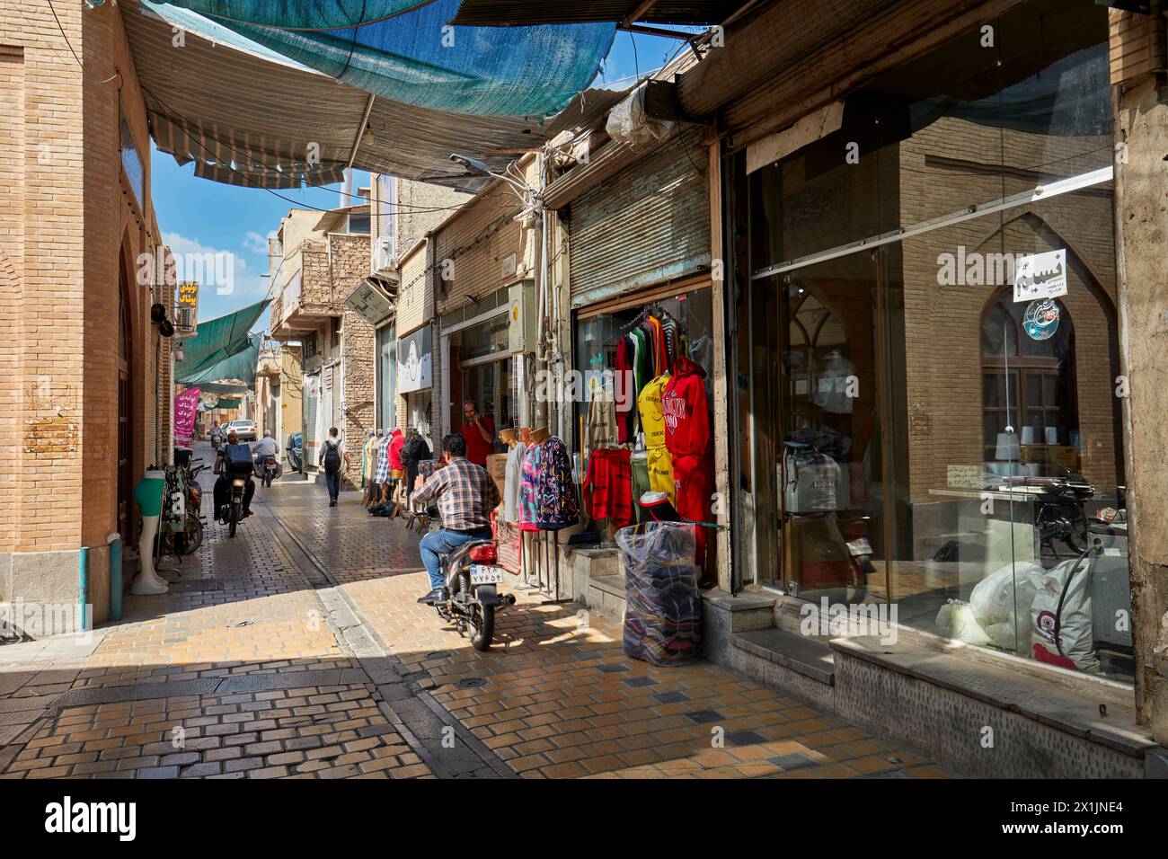 A narrow cobbled street with sun shade canopy lined with small shops in the historic center of Isfahan, Iran. Stock Photo