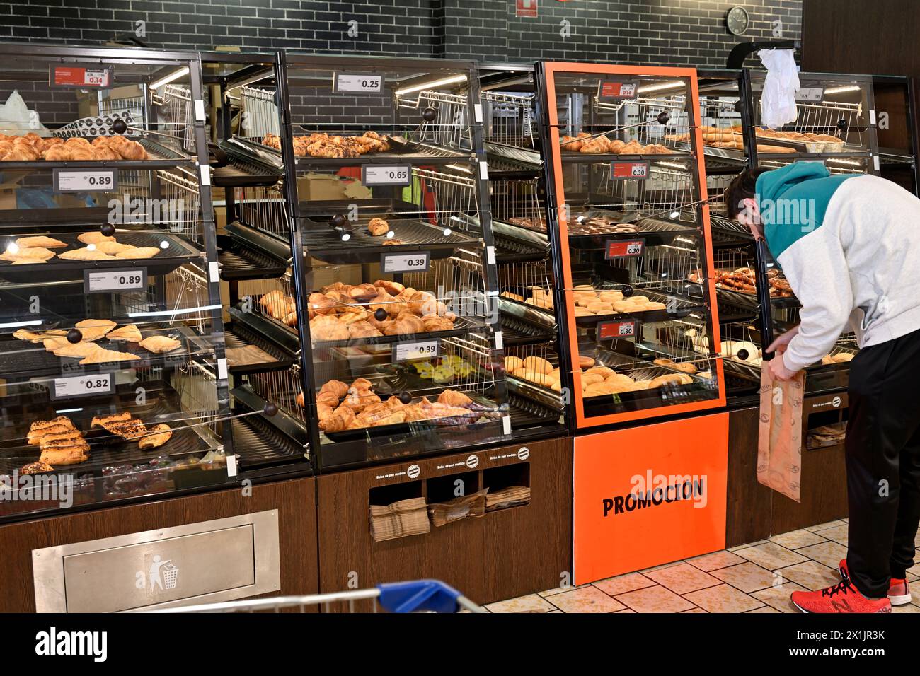 Customer selecting pastries and snacks from self service bins which prevent handling in supermarket Stock Photo