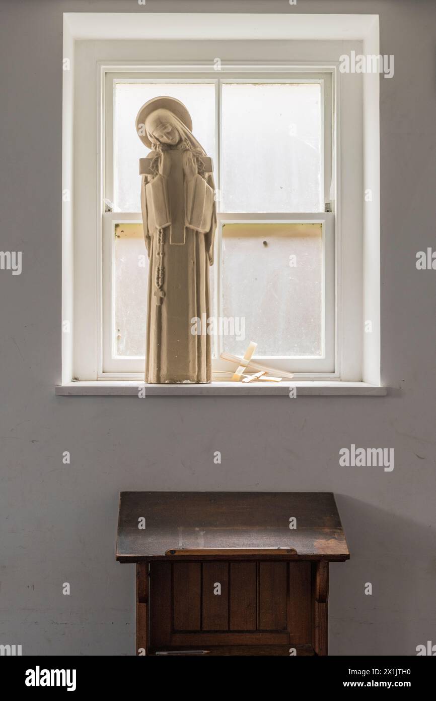 A prie-dieu or prayer desk in a quiet room beneath a window, with a statue of the Virgin Mary and two palm crosses Stock Photo