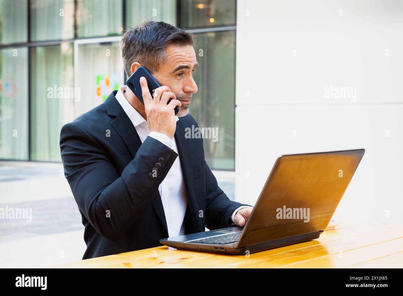 Businessman working with laptop and talking on smartphone smiling outdoors. Stock Photo