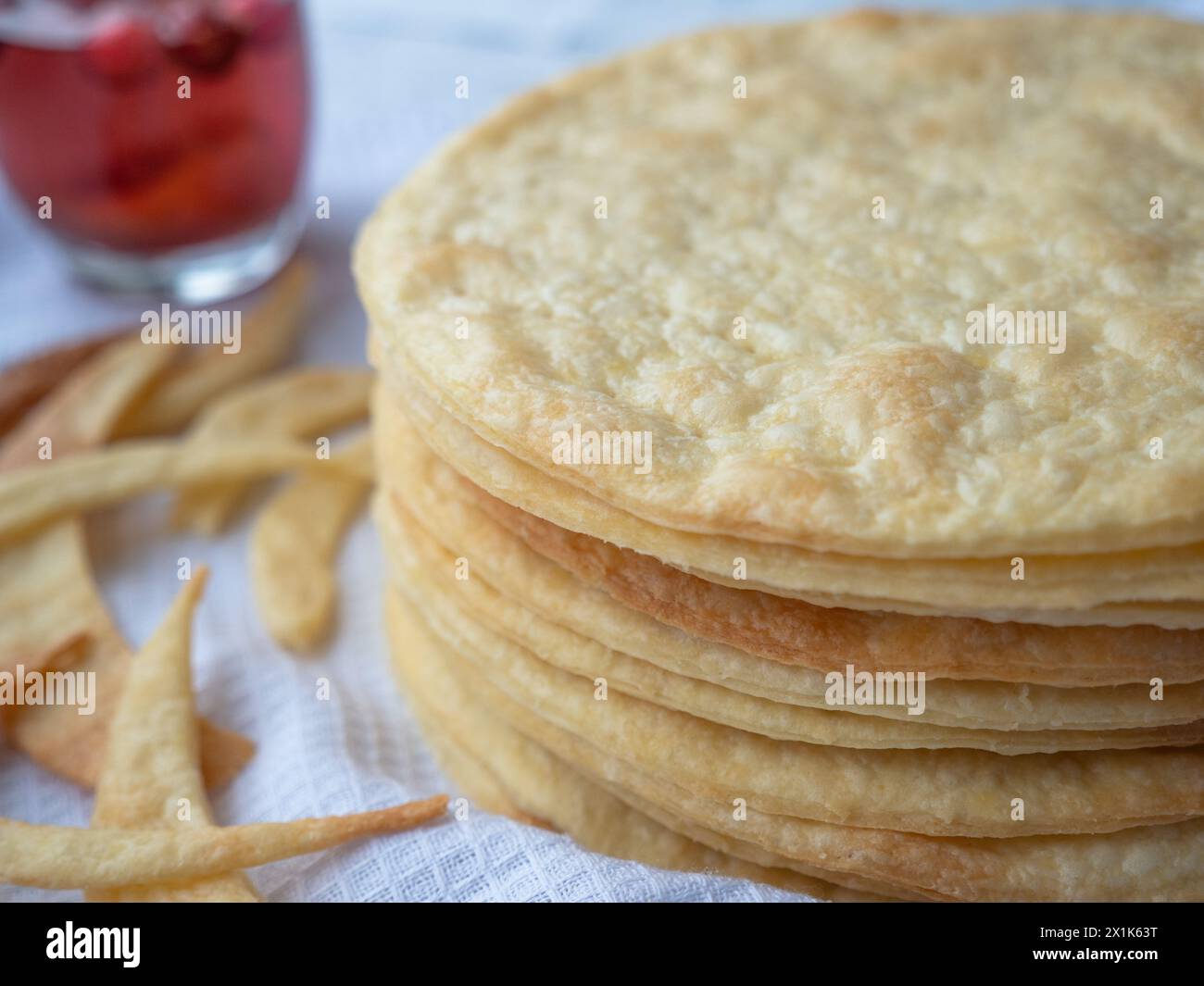 A pile of baked thin round buttery layers, dough scraps on a white waffle towel ready to make shortcrust puff pastry Napoleon cake. Red glass behind. Stock Photo