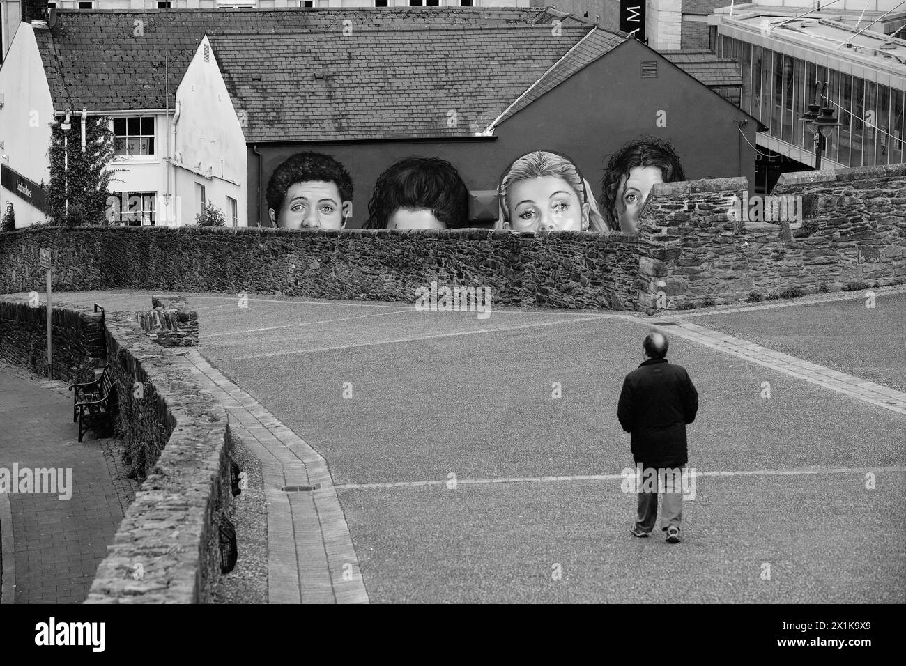 Man walking on the city walls of Derry/Londonderry, Northern Ireland with a mural of the English/Irish TV series mural Derry Girls in the foreground. Stock Photo