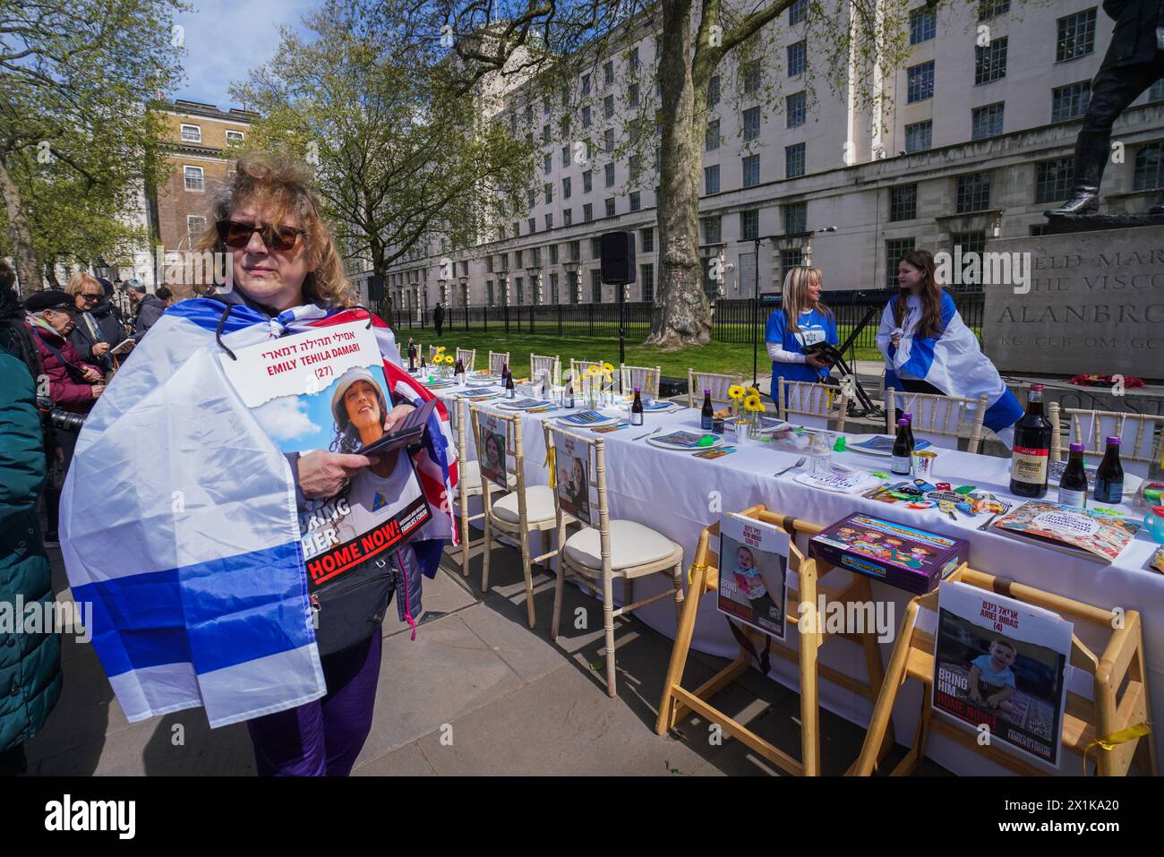 London 17 April 2024 .  A woman draped in an Israeli flag holds a picture of a hostage. Empty tables that  are set up in Whitehall  opposite Downing Street  with the names, ages and photos symbolising the  130 Israeli hostages  that  are  still being held in Gaza by Hamas .Credit: amer ghazzal/Alamy Live News Stock Photo