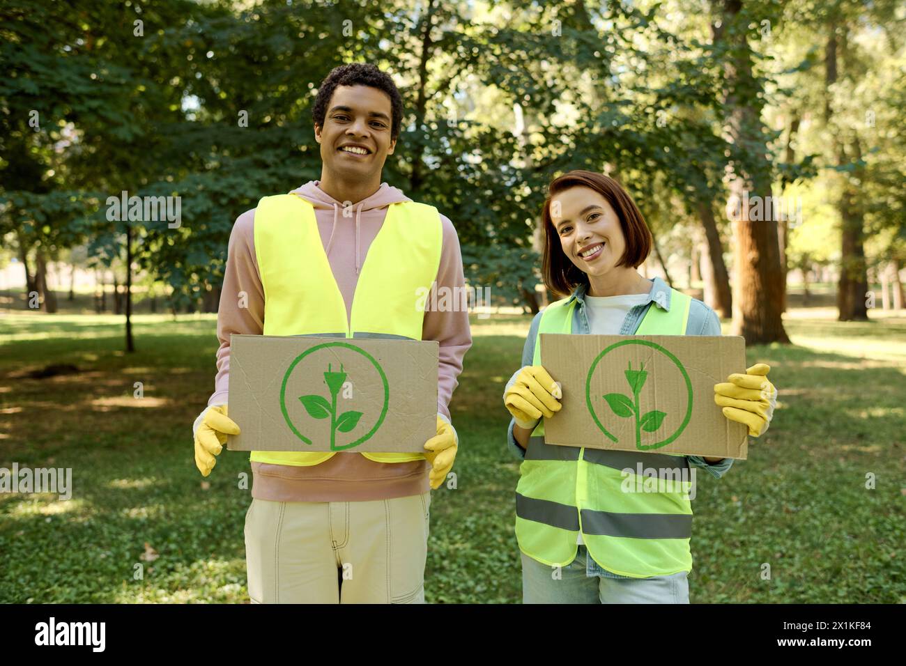 African american man and woman in safety vests holding up cardboard signs, advocating for a cause at a park cleanup event. Stock Photo