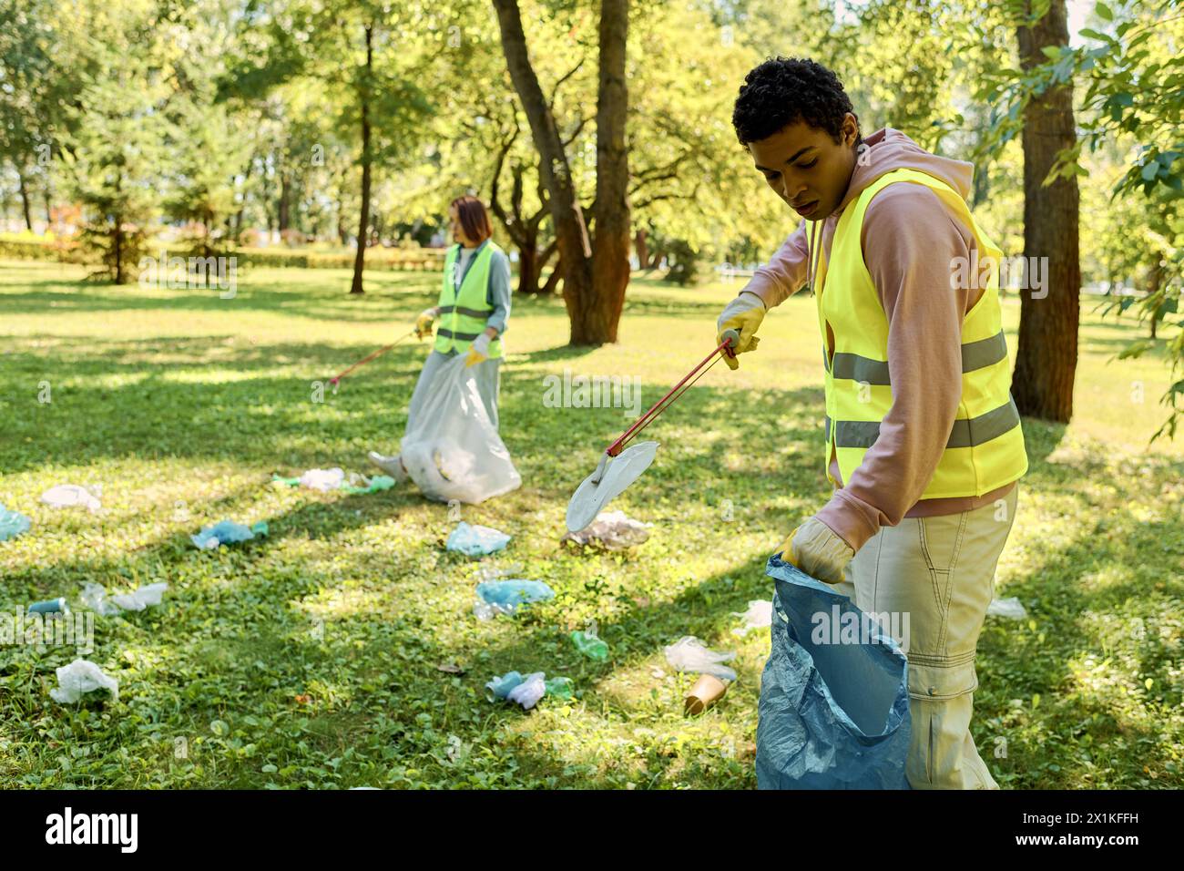 Diverse couple in a vibrant yellow vest tidies the grass in a park with care, embodying the spirit of environmental stewardship. Stock Photo