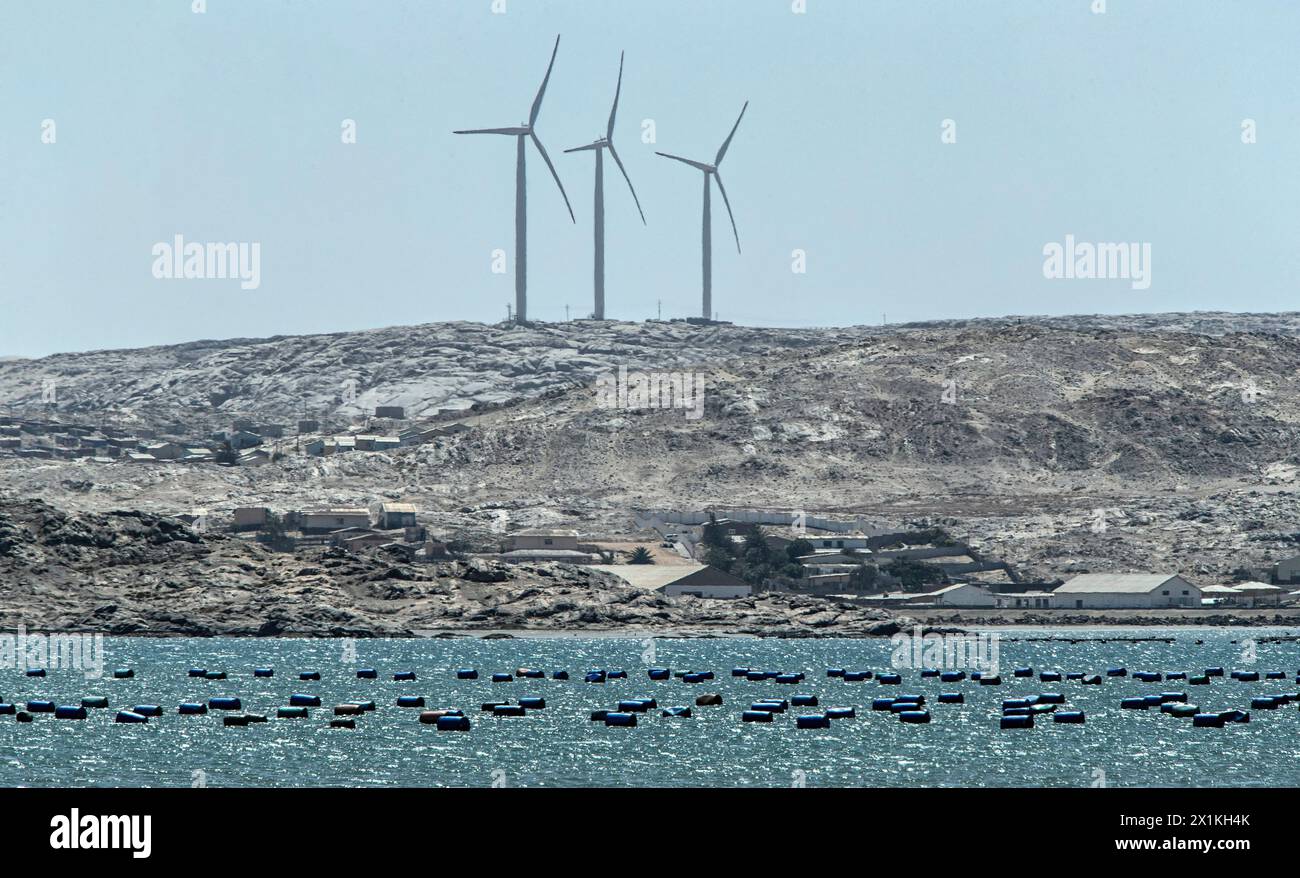 Three wind turbine towers on the rocky hillside, above the town and the