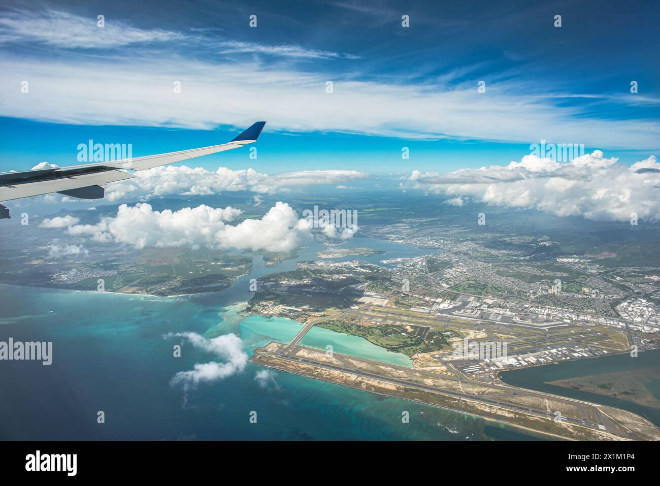 'Above the Horizons: An aerial vista captures Oahu, Hawaii, with the airport below, framed by billowing clouds, a vast expanse of blue sky, and the di Stock Photo