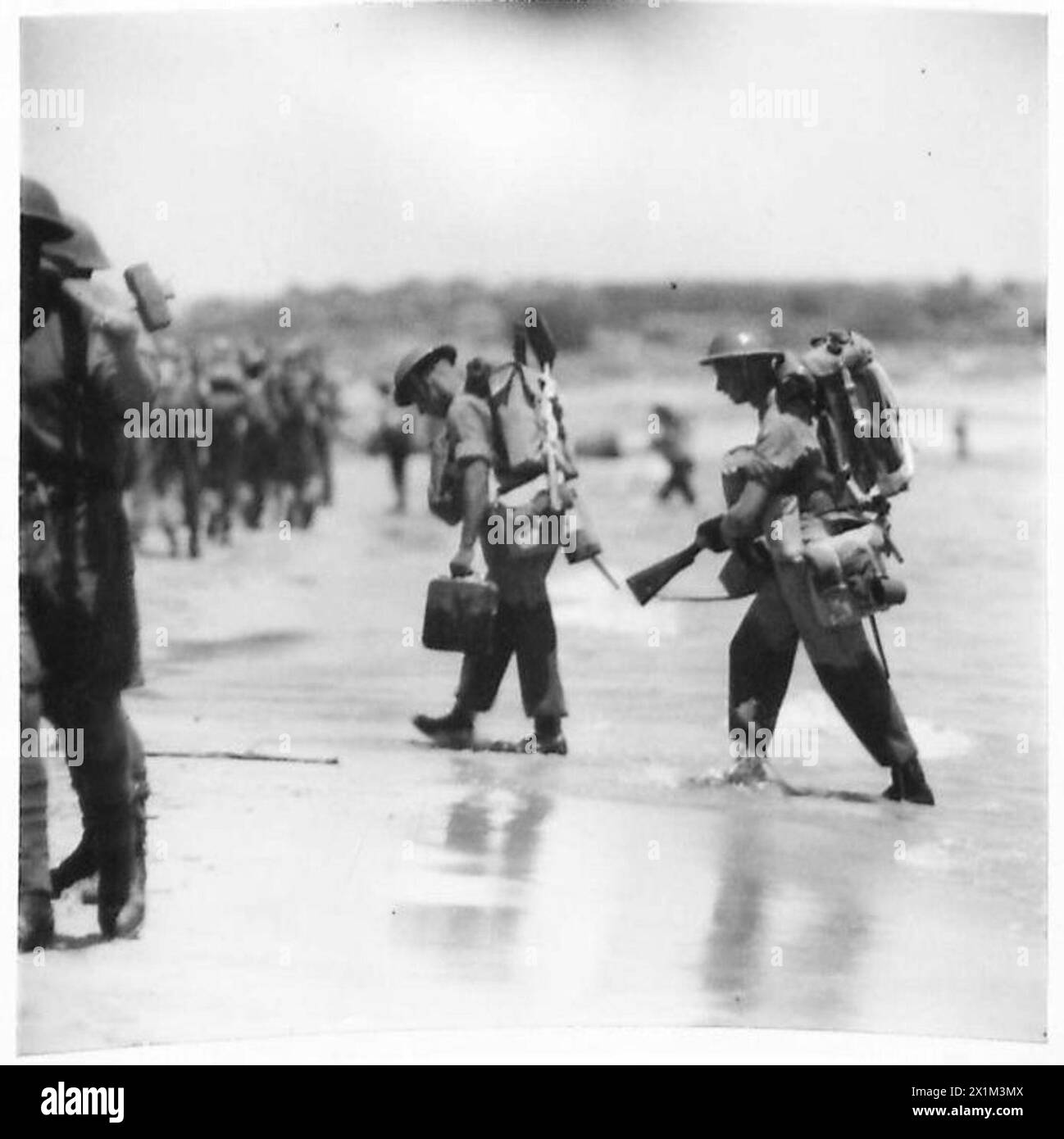 Two British soldiers disembark from shallow water onto a Sicilian beach ...