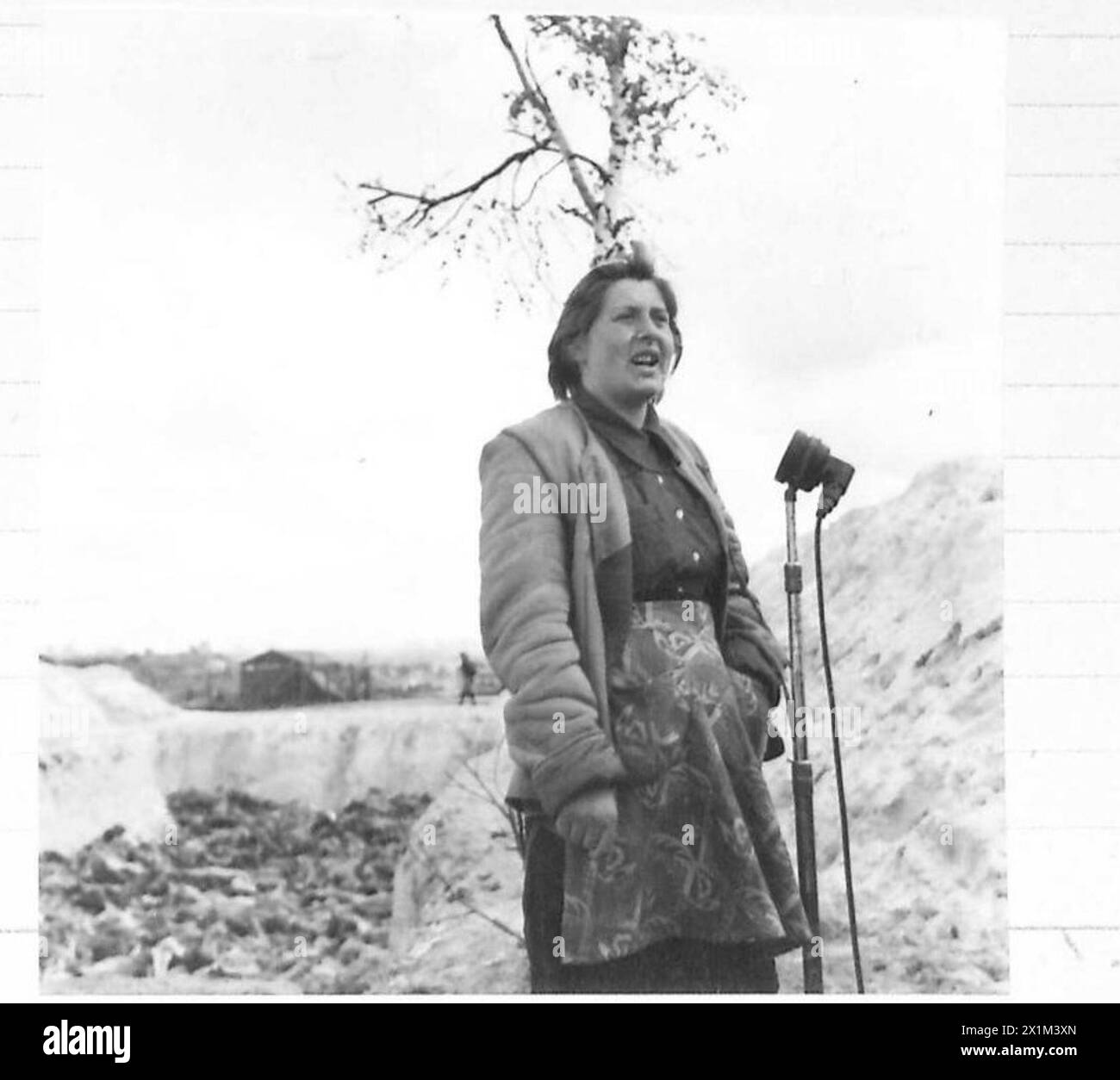 THE LIBERATION OF BERGEN-BELSEN CONCENTRATION CAMP, APRIL 1945 - Hela Goldstein, a Polish inmate, speaking for the Movietone News about her suffering - being born in a Jewish family, which meant four years in concentration camps, 21 April 1945.Born in Tuszyn in central Poland, she was in Łódź (Litzmannstadt) Ghetto, Auschwitz and Bergen-Belsen camps (in Belsen only for two weeks before British troops arrived). A mass grave full of dead inmates can be seen in the background, Goldstein, Helena Stock Photo