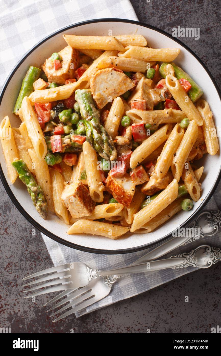 Penne pasta with chicken, asparagus, bell peppers and green peas in a creamy chipotle cheese sauce closeup in the bowl on the table. Vertical top view Stock Photo