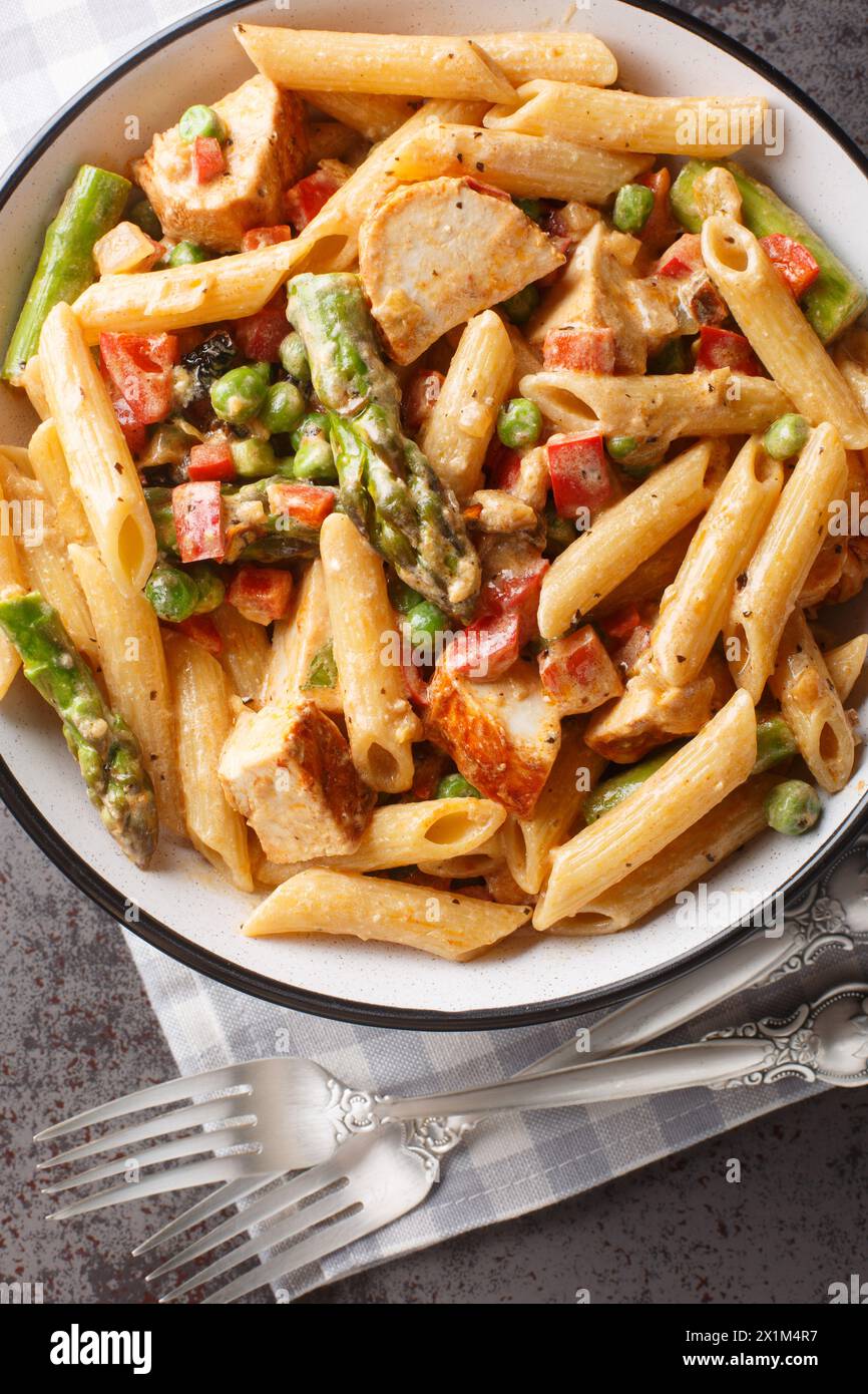 Spicy Chicken Chipotle Pasta with asparagus, bell pepper, green pea and onion closeup in the bowl on the table. Vertical top view from above Stock Photo