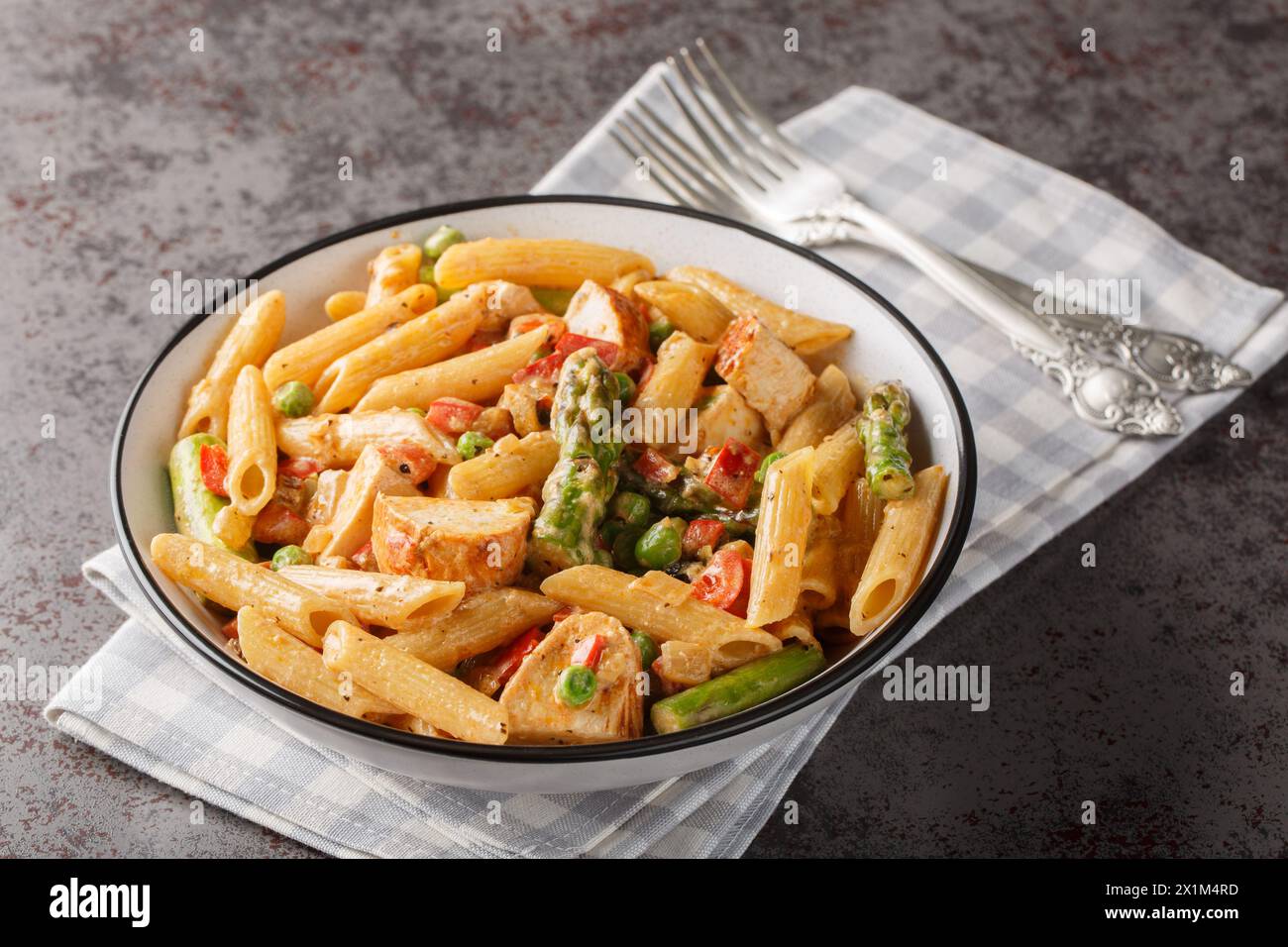 Creamy chipotle chicken penne pasta with asparagus, peppers, green peas, onion and garlic close-up in a bowl on the table. horizontal Stock Photo