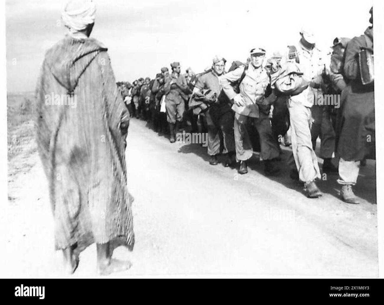 An Arab observes a large group of prisoners being escorted to cages ...
