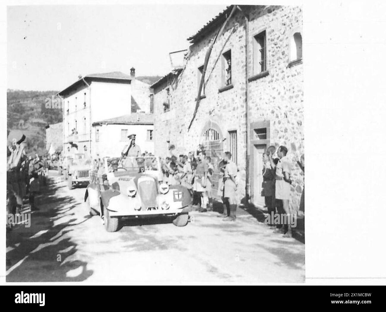 His Majesty the King passes through a small village in a royal car while troops of the Eighth Army line the roadside and cheer, British Army. Stock Photo