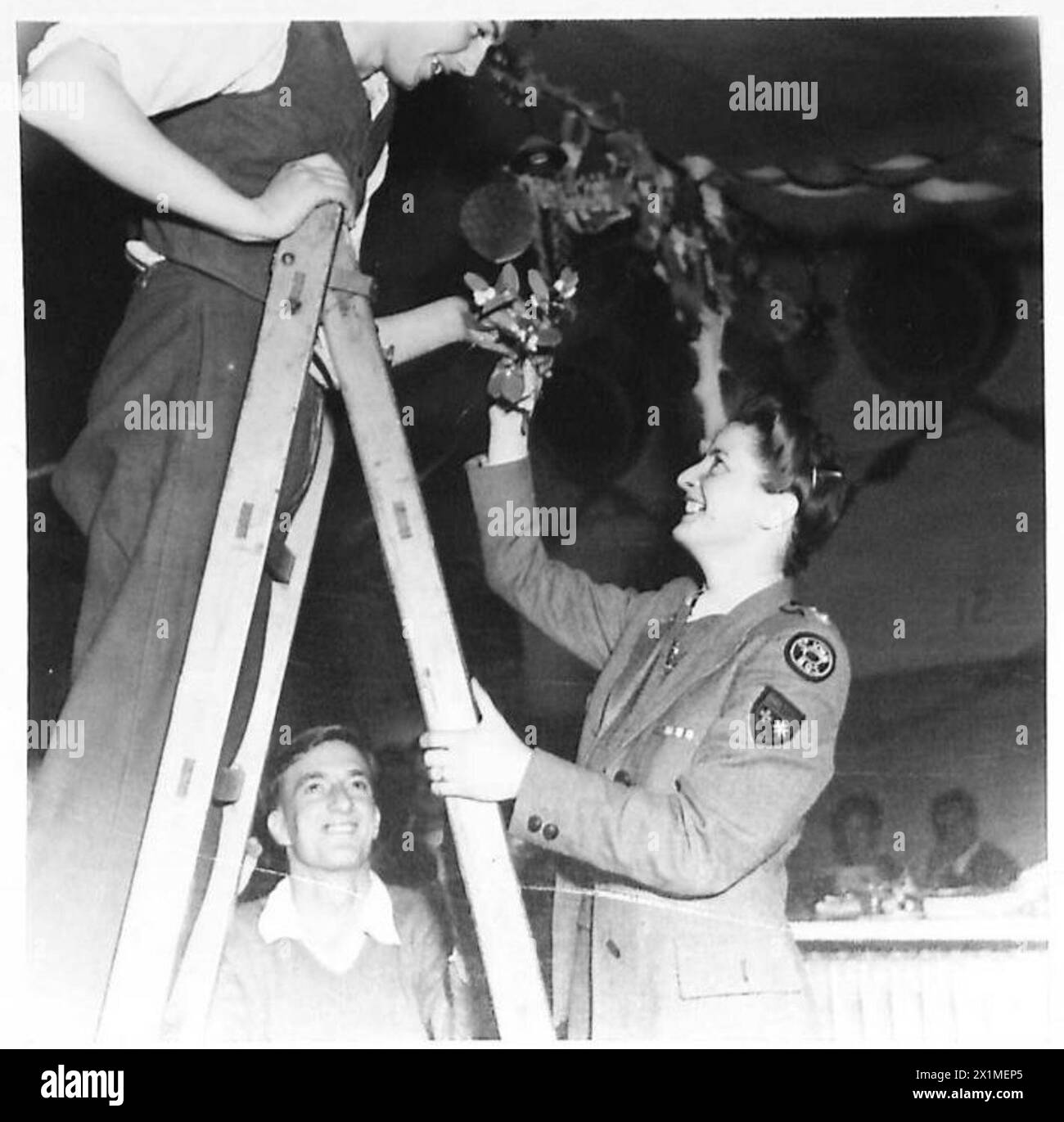 CHRISTMAS DECORATIONS - Mrs. Majorie Oxford of Bristol, British Red Cross (St.Johns) hands a sprig of mistletoe up to Fus. Donald Ryder of Sunnyhill, Preston Brook, Warrington, Lancs, who is on the ladder fixing decorations in the hospital ward, British Army Stock Photo