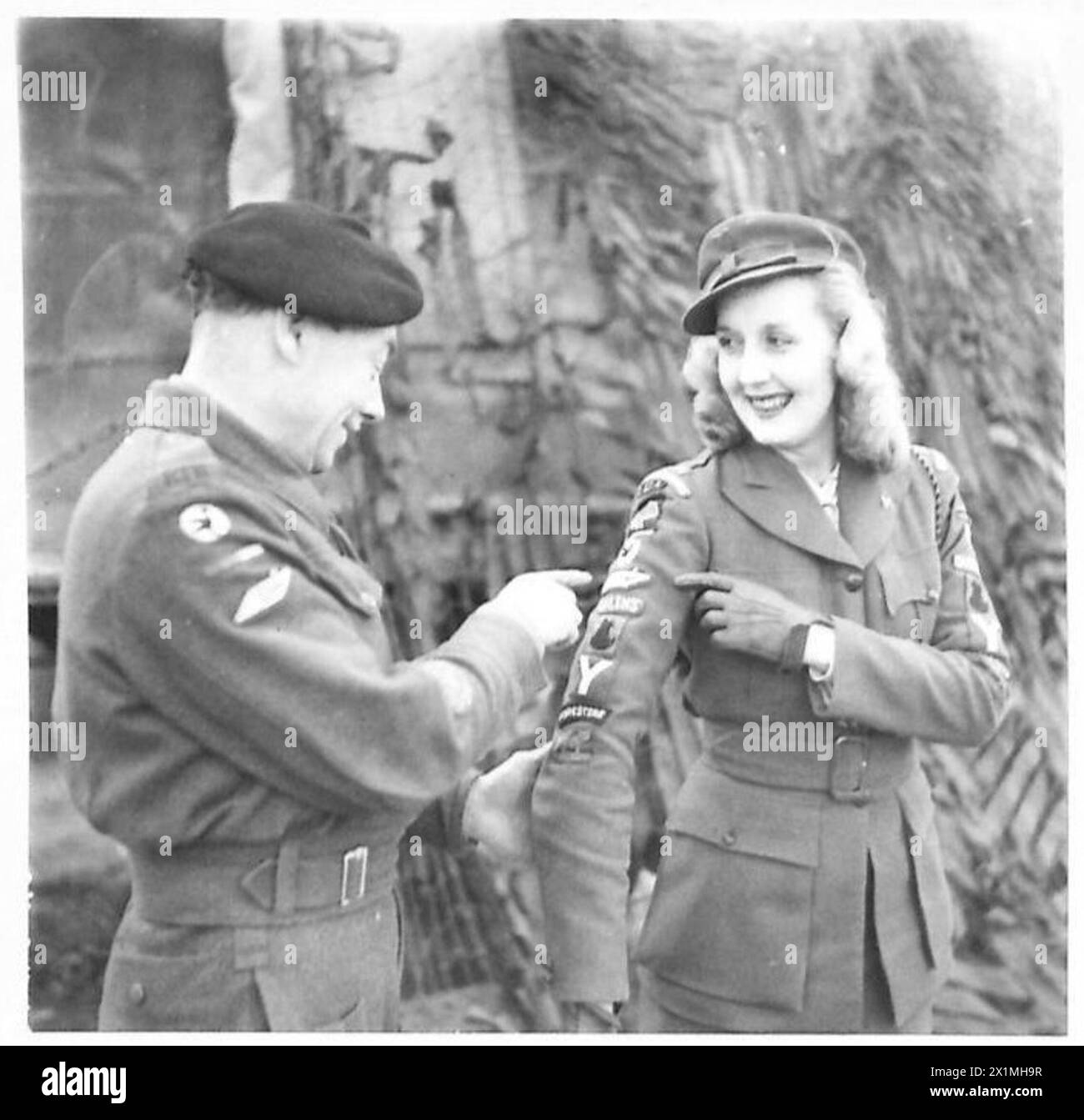 CANADIAN SINGER ENTERTAINS TROOPS - Miss Inga Andersen, known as Canada's Sophisticated Songstree, and who has been giving shows with her accompanist, Hal Chambers, to the forward troops in Italy. RQMS H. Clare, 40 Bn. R.T.R - of 50 Out Lane, Woolton, Liverpool, inspects the regimental and divisional badges and signs given to Miss Andersen by the various units for whom she has sung. Each Division represented by the badges on Miss Andersen's arms have adopted her as their 'Forces Sweetheart', British Army Stock Photo