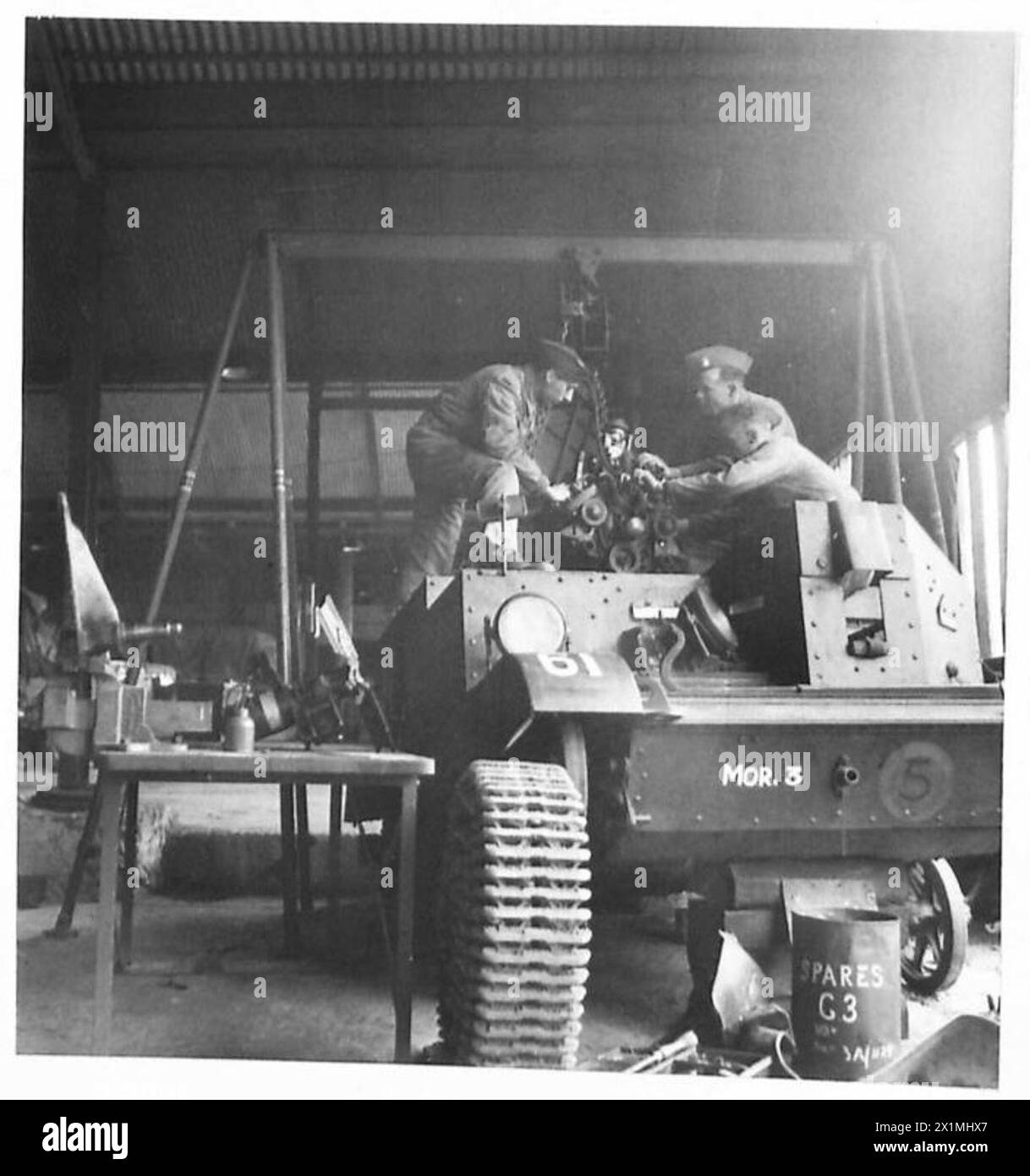 THE ACTIVITIES OF THE ROYAL ELECTRICAL AND MECHANICAL ENGINEERS - Putting an engine into a Bren carrier. Left to right - Craftsman Erselius of Holloway, London, was a truck driver. L/Cpl. H. Roberts of Northwich, Cheshire a grocery salesman. Sgt. W. Wallis of New Malden, Surrey a Stores Manager, British Army Stock Photo