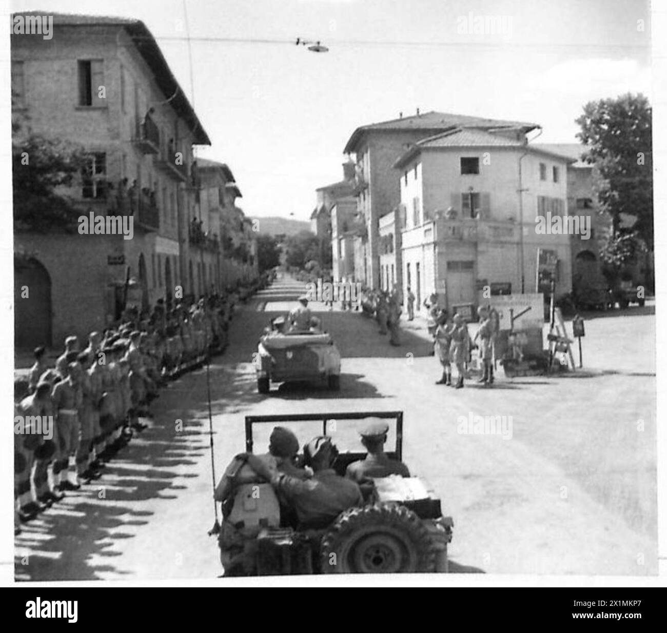 The King passes in his royal car along a roadside where troops of the Eighth Army are drawn up, cheering during the visit, conducted by the British Army. Stock Photo