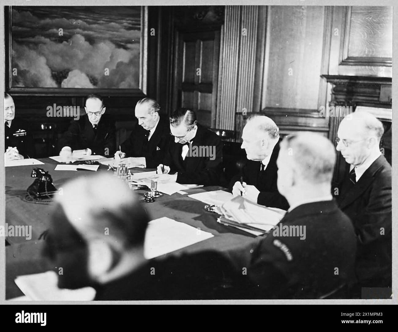 SIR ARCHIBALD SINCLAIR SIGNS THE EXTENSION OF THE EMPIRE AIR TRAINING SCHEME - (Picture issued 1943). 9160. The Rt.Hon sir Archibald Sinclair [centre] signing the Agreement. Left to right are - Air Vice Marshal H.N. Wrigley [Air Officer Commanding Overseas HQ R.A.A.F.] The Rt.Hon. Vincent Massey [High Commissioner for Canada] The Rt.Hon. S.M. Bruce [High Commisioner for Australia] Mr. W.J. Jordan [High Commissioner for New Sealand] Mr. L.J. Banford [Secretary] Air Commodore A. de T. Nevill [Air Officer Commanding R.N.A.F. HQ London] Mr. R.M.Campbell [Official Secretary, Office of the High Comm Stock Photo