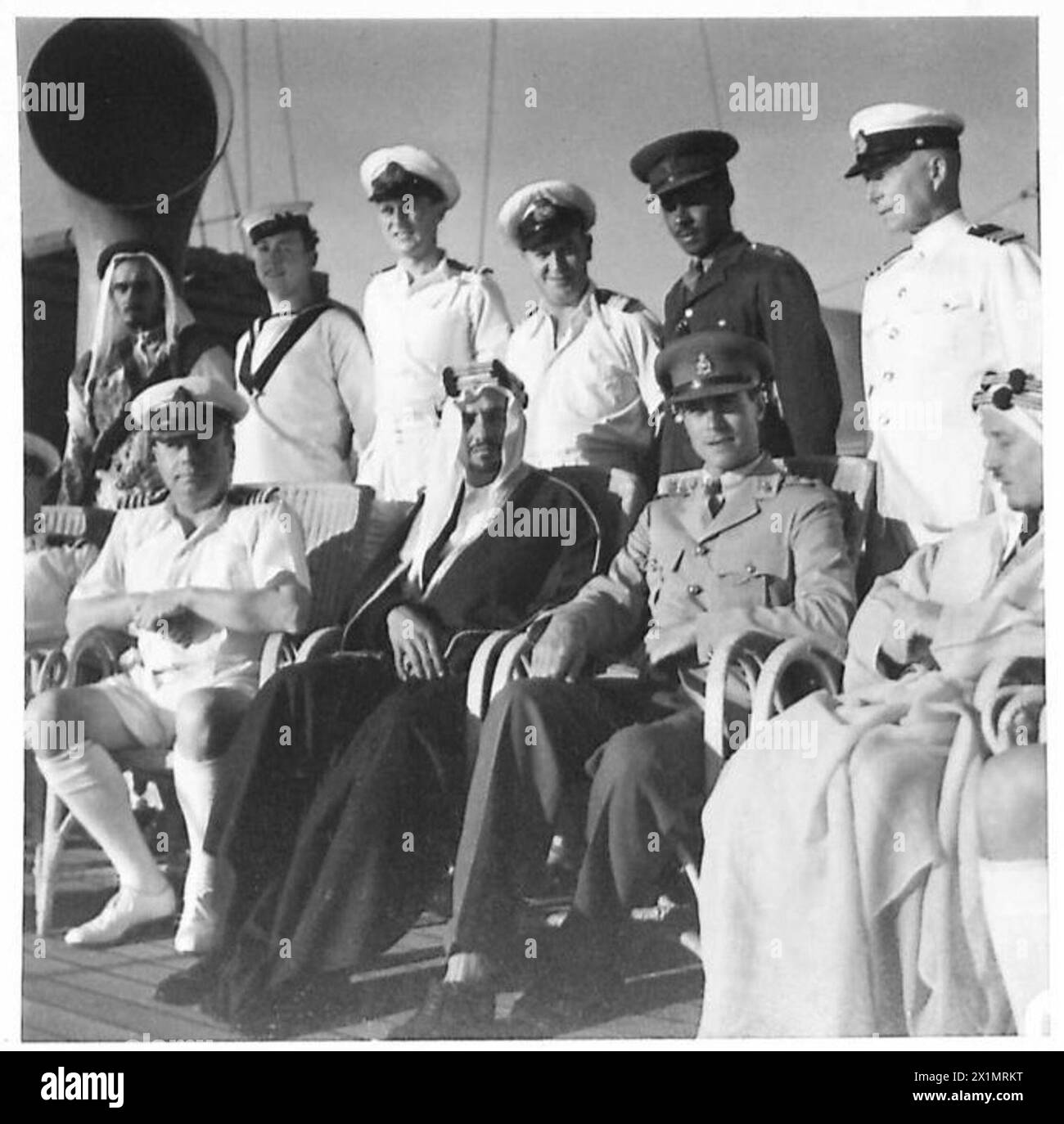 TOUR OF HRH EL EMIR MANSUR IBN SAUD - A group on deck. From left to right:-Back Row: A body-guard, A Naval Able Seaman, Lieutenant D A Holbrook NR, Purser W H Powers, Lieutenant M Diab Interpreter, Chief Engineer of the ship W Neilson, a Naval Able Seaman, a Body-guard.Front Row: Captain L C Barry RN, Captain C B Barry, DSO. RN, in charge of Naval Escort, His Royal Highness Emir Mansur bin 'Abd al-'Aziz, Captain P A Uniacke, acting as Liaison Officer, Dr Midhat Sheikh Al Ardh, Medical Adviser of HHR Emir Mansur bin 'Abd al'Aziz, Lieutenant Commander R M Marshall, RNVR Medical Officer, Stock Photo