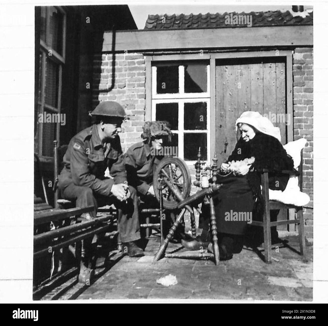 WITH THE BRITISH TROOPS IN HOLLAND. - Dvr. Hutton, J of Manchester and Gnr. Brazier, H.J. of Shifnal, Shropshire, both of the 75 A/Tk Regt., watch with great interest an old Dutch lady, 83 years of age, at work on an old spinning wheel, British Army, 21st Army Group Stock Photo
