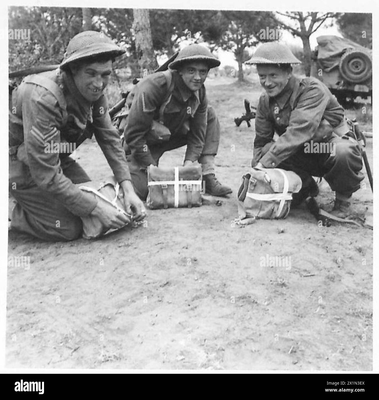 FIFTH ARMY : ANZIO OFFENSIVE - White tapes are tied in a cross onto the back pack of each man in order to help the men following in the darkness to keep on the correct path. Three Middlesborough men arrange their tapes. They are - left to right - Cpl. J. Tierney of 16 Nelson Street, West Hartlepool, L/Cpl. G. Dowson of 3 Emerald Street, Middlesbrough Sgt.P. Maher, 80 Middlesbrough Road,Southbank, Middlesborough , British Army Stock Photo