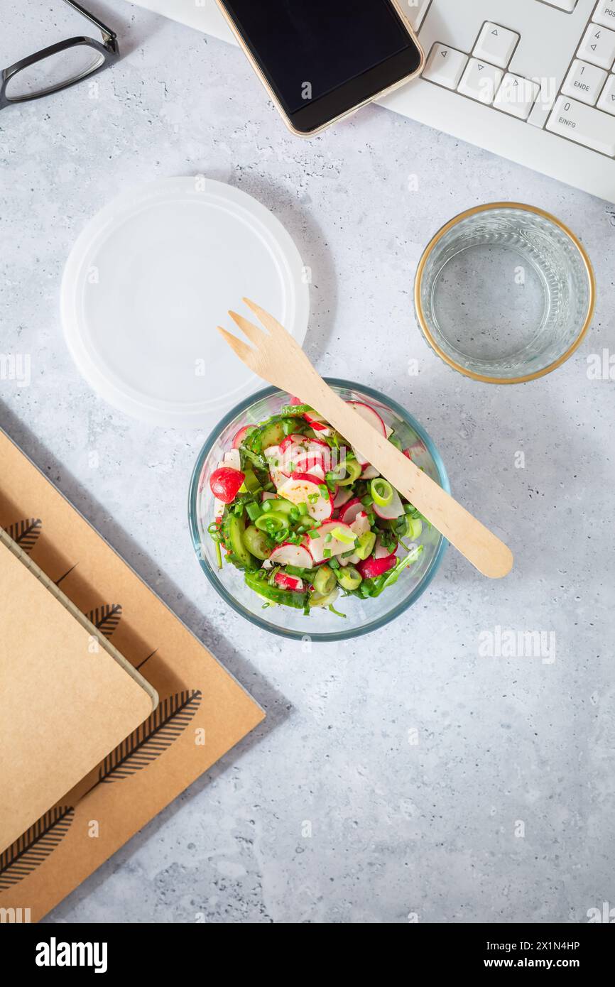 Healthy food in a office. Prepared radish and cucumber salad on  a desk with office supplies Stock Photo