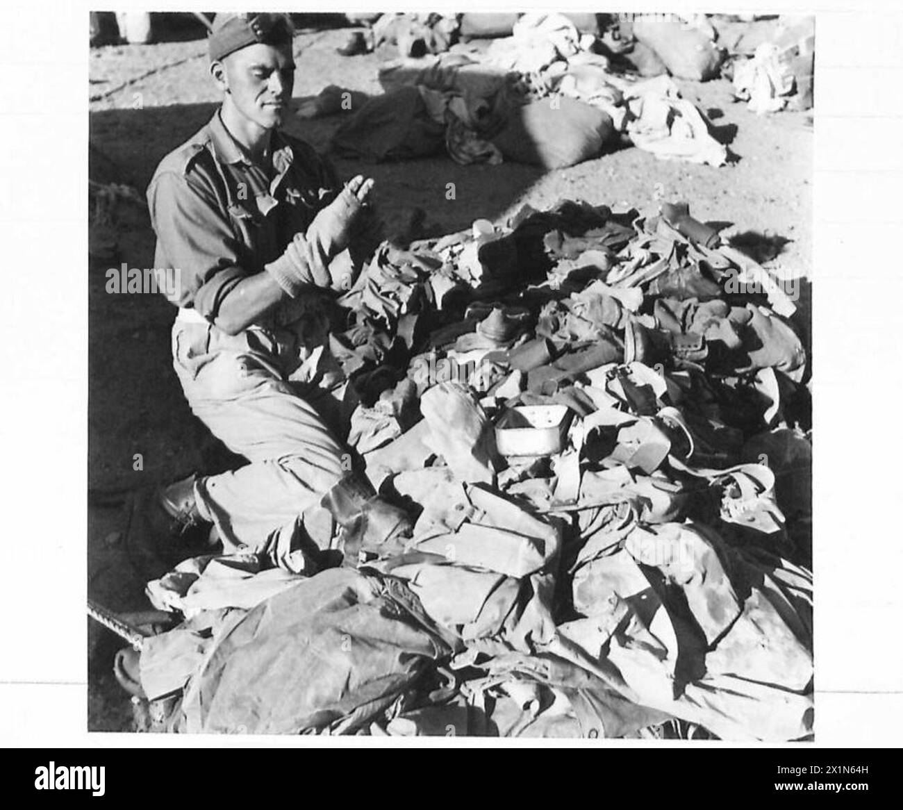 BRITISH EXPEDITIONARY FORCE TO FIGHT LOCUSTS IN THE MIDDLE EAST - From a pile of discarded clothing on the salvage heap, Pte. Moorhouse of Brierfield, Lancs takes a pair of socks and wonders if they could be mended, United Nations Organisation [UNO] Stock Photo