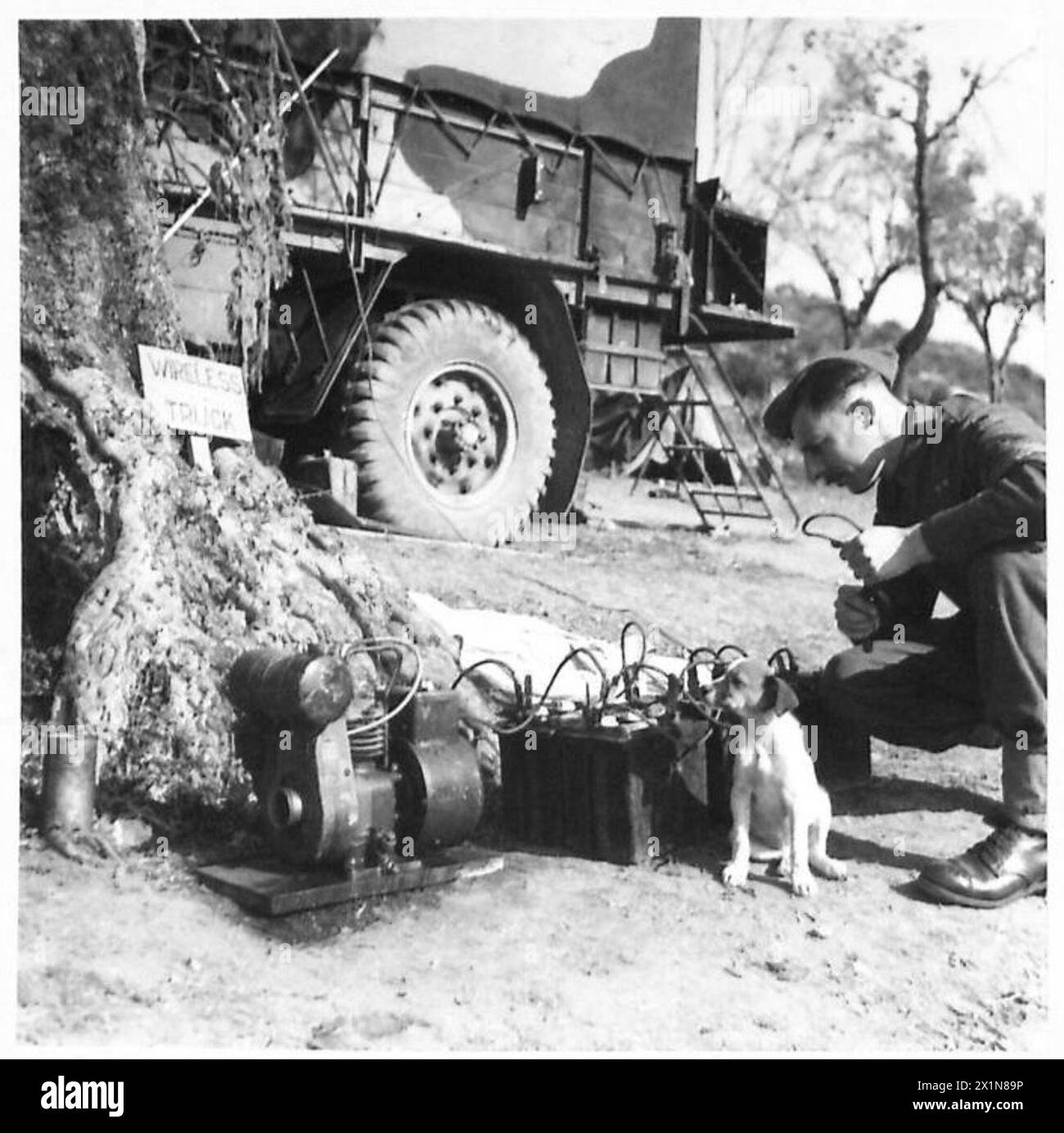 ITALY : FIFTH ARMYWIRELESS REPAIR SECTION : REME - S/Sgt. R.L. Jerome testing batteries that are being charged by a 12-volt output generator. Beside him is the dog mascot 'Gemma', British Army Stock Photo