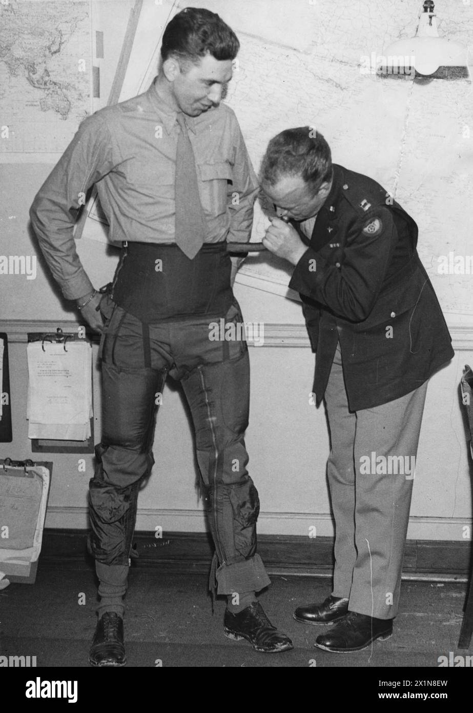 UNITED STATES EIGHTH AIR FORCE IN BRITAIN, 1942-1945 - Lieutenant Donald W. Johnson, pilot of the 339th Fighter Group, watches on as Captain Charles D. Nethaway demonstrates how the 'G-suit' worked.'G-suits' were developed to counter the blackouts that pilots suffered when the G-force on their bodies during tight turns forced the blood from their brain to the lower part of their body. Inflated by the exhaust of the P-51 Mustang's vacuum system, the suits applied pressure to the pilot's legs and abdomen, forcing the blood to continue to circulate around the upper body. The suits were issued to Stock Photo