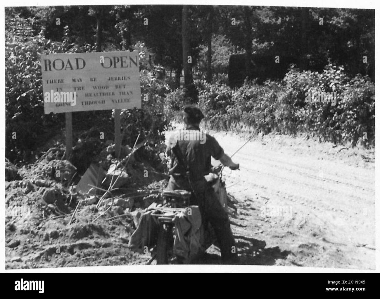 NORMANDY - VARIOUS - Motor cyclist reads a road sign that says 'Road Open - there may be Jerries in the woods but it is healthier than going through Vallee', British Army, 21st Army Group Stock Photo