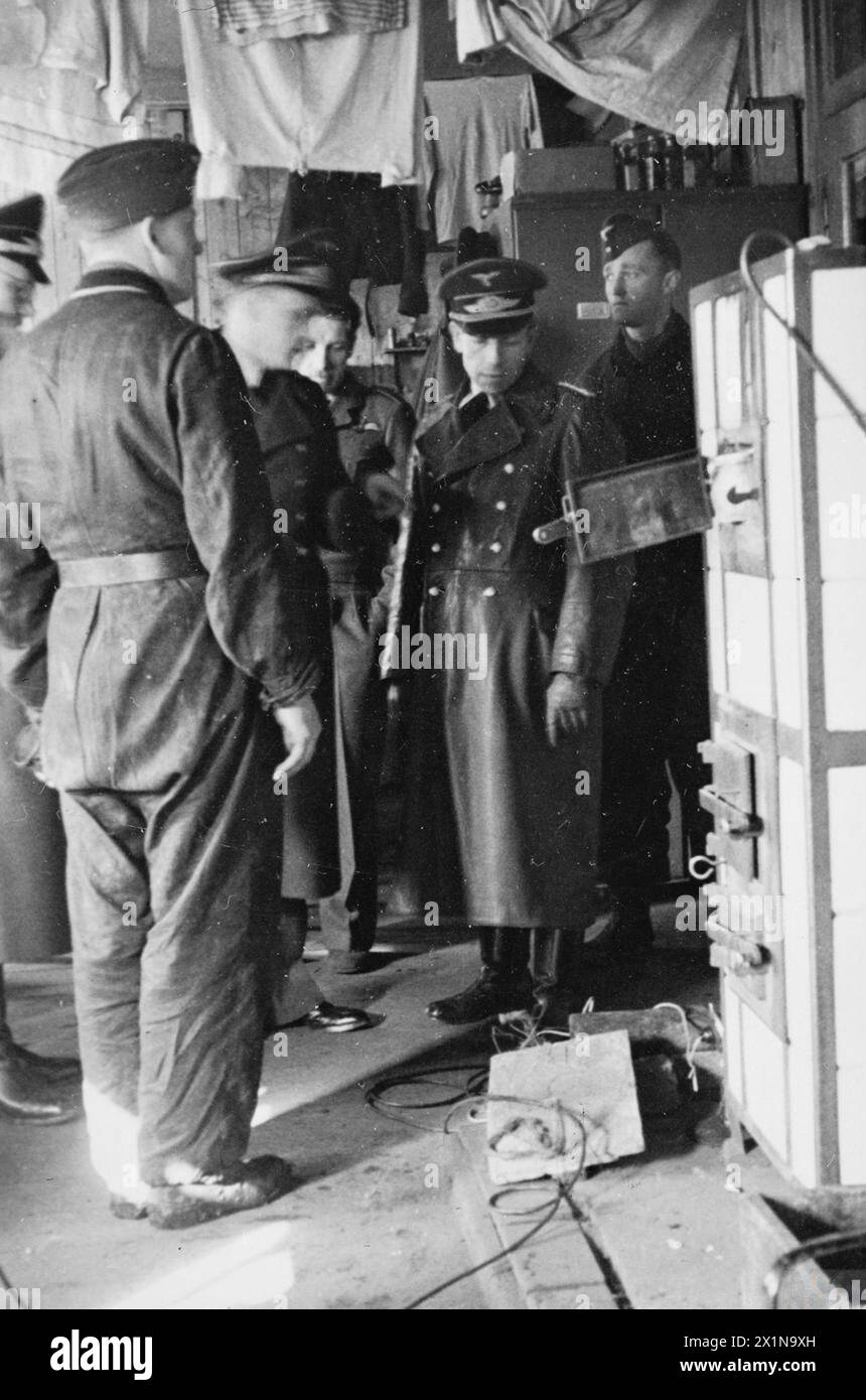 STALAG LUFT III AND THE 'GREAT ESCAPE' - A group of German officers looking at the entrance to an earlier tunnel dug by POWs under a stove at Stalag Luft III, Sagan. It is believed to be in Block 56 of the Centre Compound. Photograph probably taken in November 1943, Royal Air Force, German Air Force Stock Photo