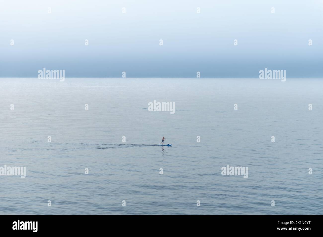 man paddleboarding on sea early sunset. A surfer enjoys a peaceful moment on his board. Stock Photo