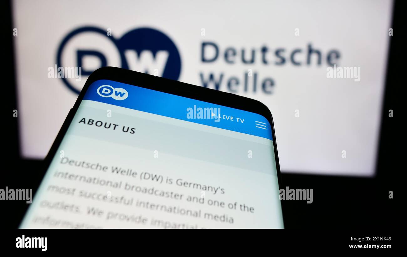 Smartphone with website of German state-owned broadcaster Deutsche Welle (DW) in front of logo. Focus on top-left of phone display. Stock Photo
