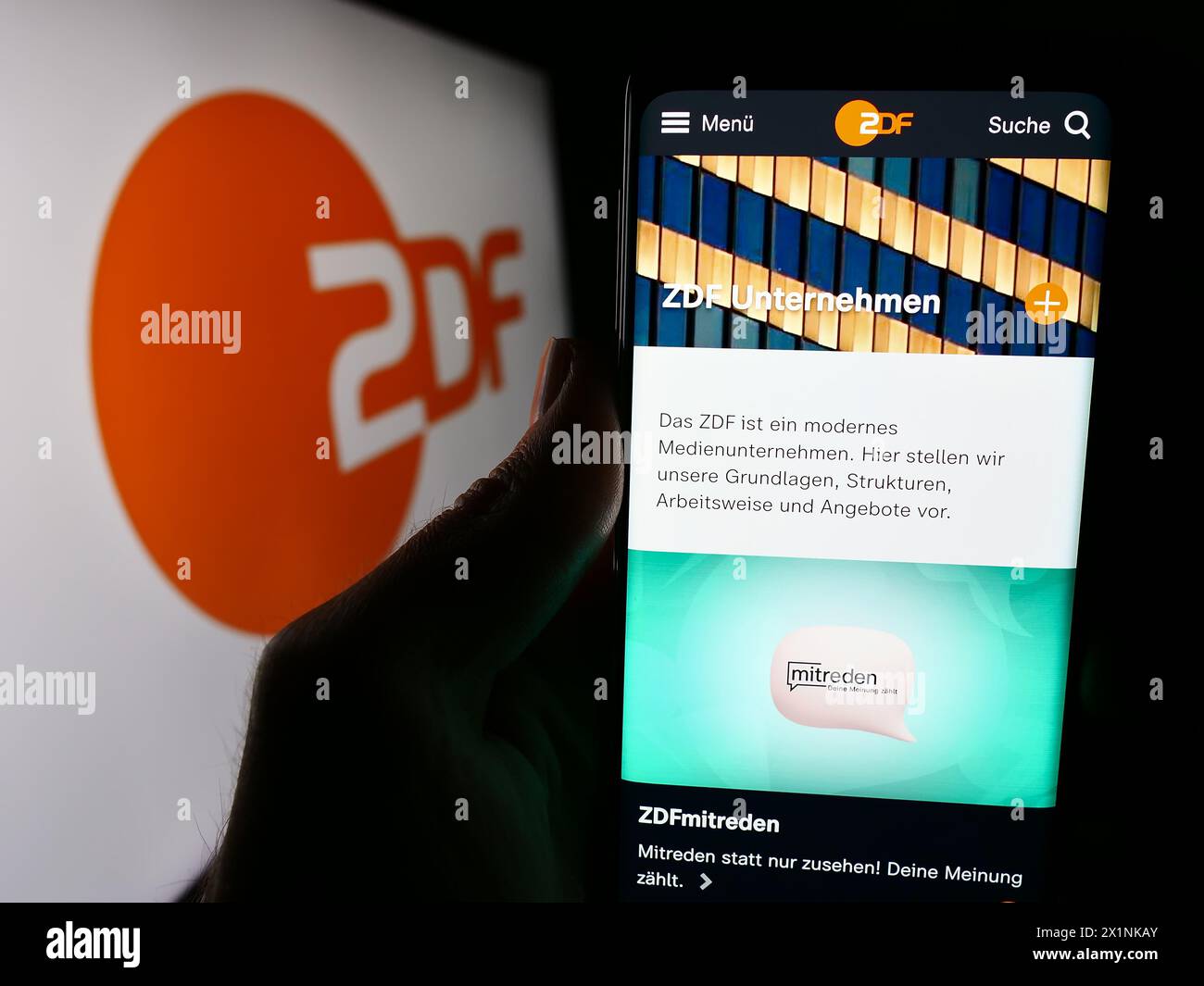 Person holding smartphone with webpage of television broadcaster Zweites Deutsches Fernsehen (ZDF) with logo. Focus on center of phone display. Stock Photo