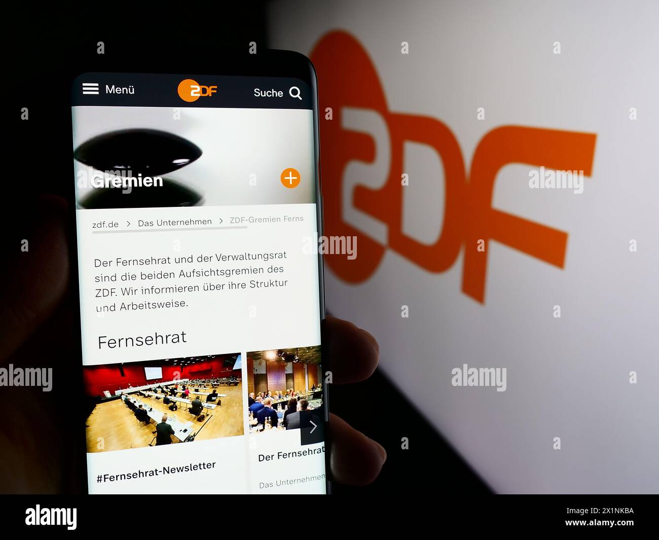 Person holding cellphone with web page of television broadcaster Zweites Deutsches Fernsehen (ZDF) with logo. Focus on center of phone display. Stock Photo