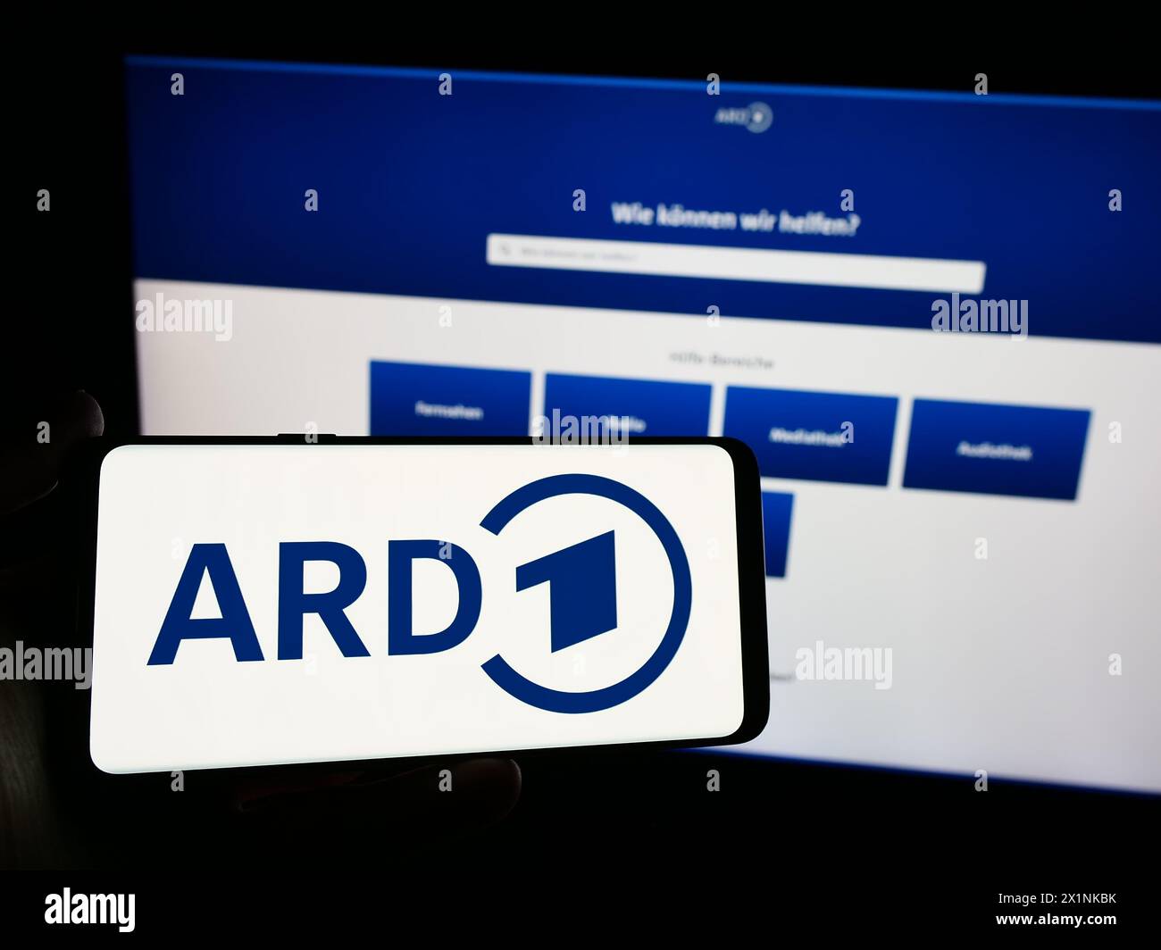 Person holding smartphone with logo of German public-service broadcasting organisation ARD in front of website. Focus on phone display. Stock Photo